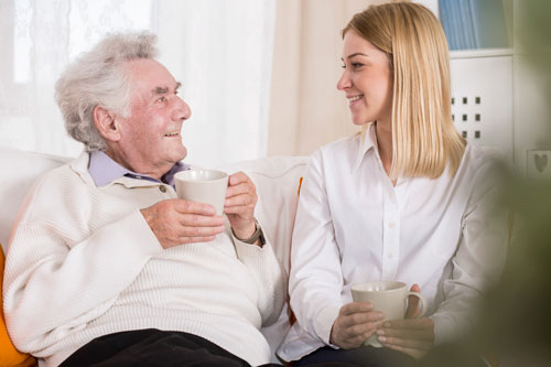 Opa und polnische Pflegekraft sitzen auf dem Sofa und lachen zusammen